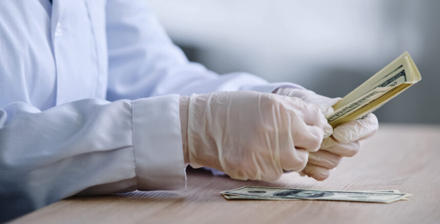 Close-up female hands in white latex gloves pharmacist doctor scientist in medical coat sits at table with bottle of pills drug counting money banknotes dollars cash salary profits from sale medicines close up hands in white latex gloves pharmacist do 2023 11 27 05 01 39 utc scaled