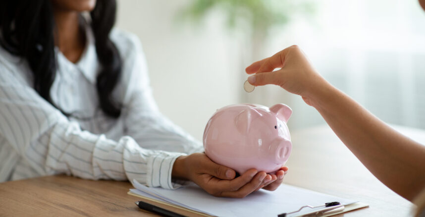 Financial planning concept. Closeup of business women putting coin into piggy bank at modern office investimentos-após-consultoria-financeira