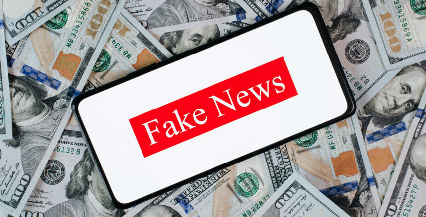 Bought news, price lies concept. Smartphone with text fake news lying on money background one hundred dollar bills, top view Celular com a frase fake news, em cima de uma pilha de dinheiro
