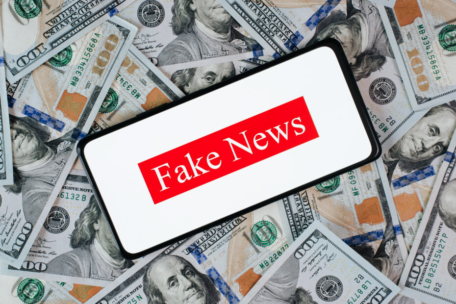 Cuidado com as Fake News Financeiras em 2025: Ganhos Fáceis e Conselhos de Quem Não Entende do Assunto 19 Celular com a frase fake news, em cima de uma pilha de dinheiro